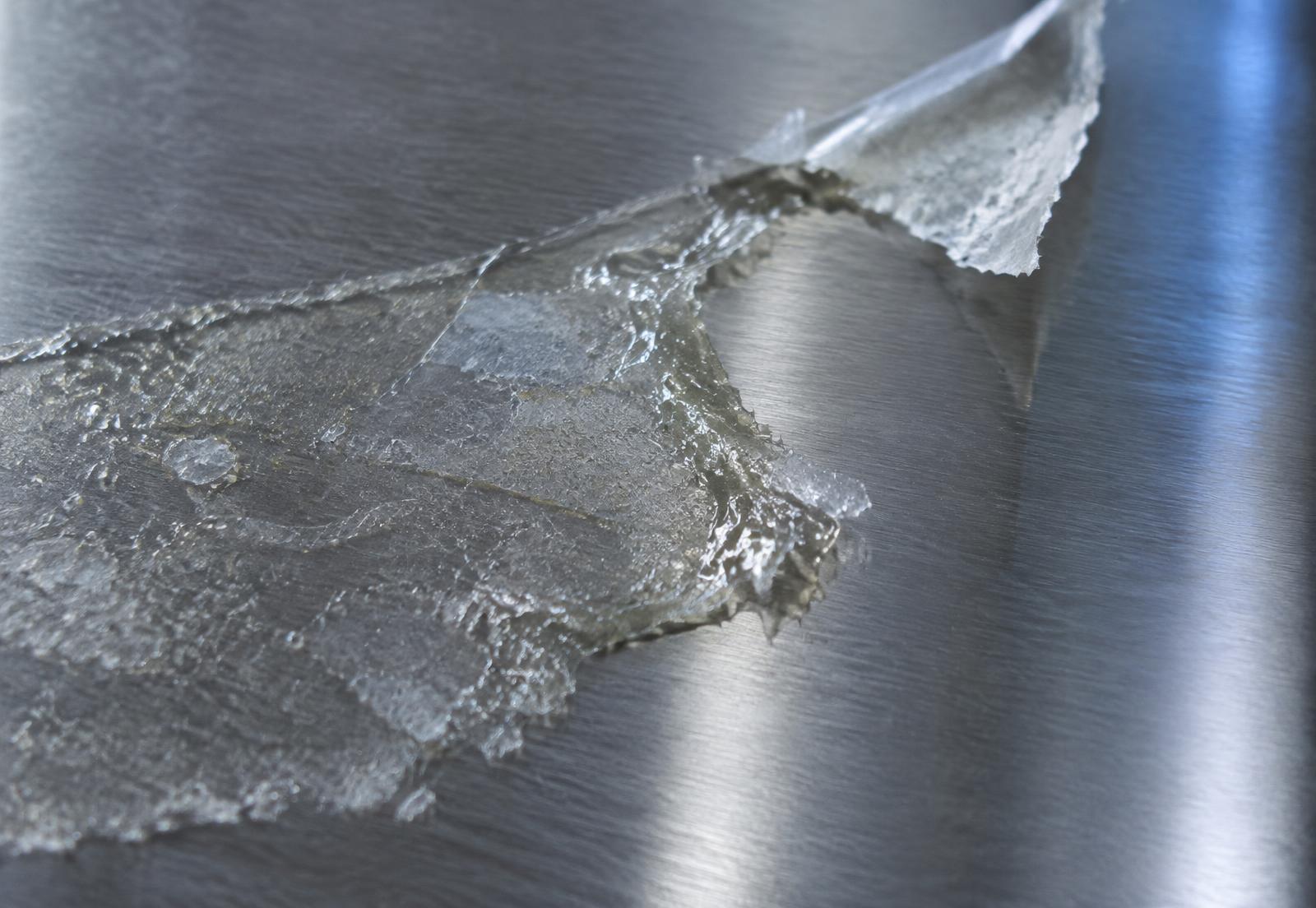 Makroaufnahme eines Kleberückstandes auf einer metallischen Oberfläche